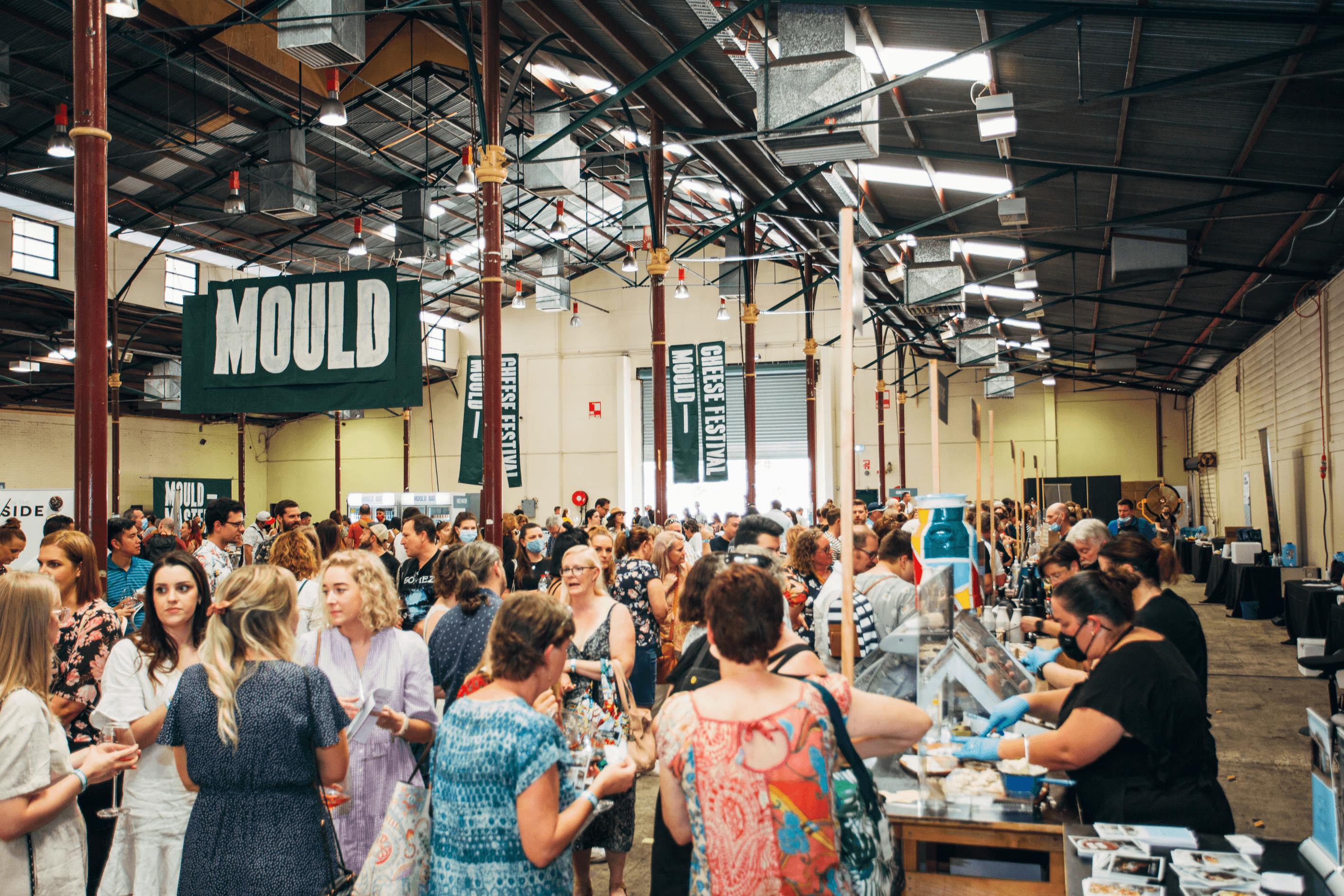 A busy hall filled with people and cheese stands.